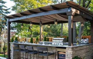 Covered outdoor kitchen with an awning, bar seating, and stainless steel appliances, creating a stylish and functional backyard cooking space.