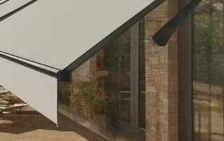 Modern house with large glass walls and a retractable fabric awning, providing shade and style for outdoor living spaces.