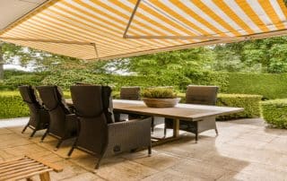 A retractable awning cools a green patio retreat—Six Reasons to Cover Your Patio with an Awning, from Best Awning Company for comfort and charm.