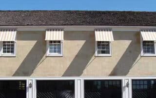Two-story house featuring striped awnings over windows and garage doors, enhancing curb appeal and functionality. Hotel Awnings Enhance Curb Appeal
